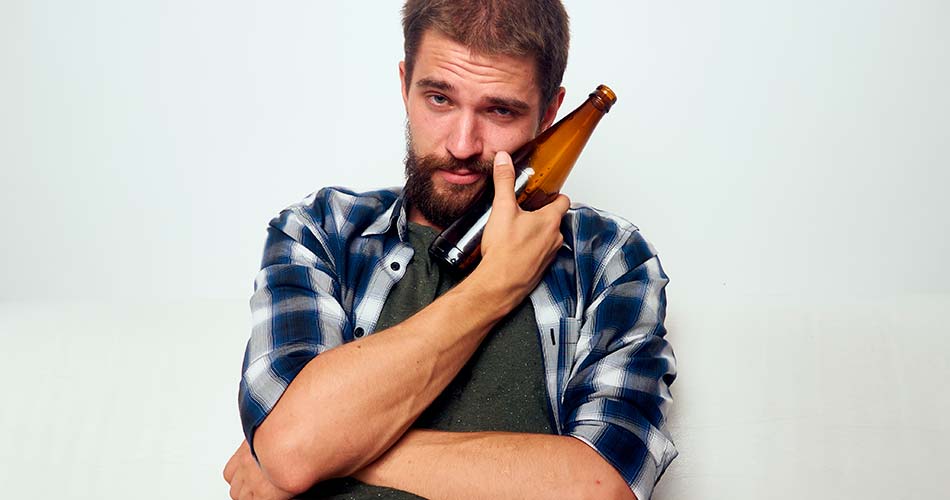 мужчина прижимает бутылку с пивом к лицу и смотрит в камеру